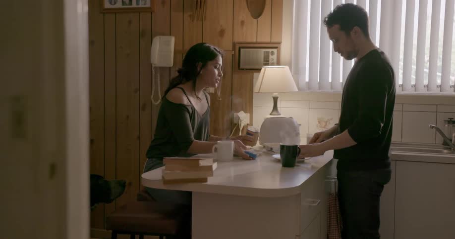 A man and woman drink coffee at a kitchen counter