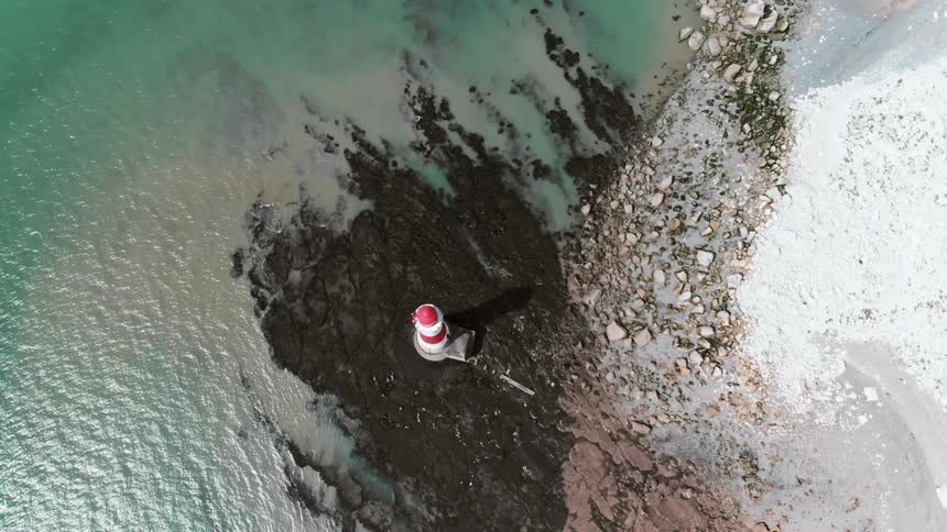 A lighthouse on the edge of the ocean is filmed from above