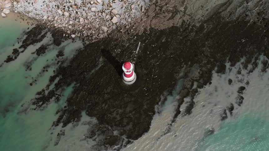 A red and white lighthouse stands on a rocky shore