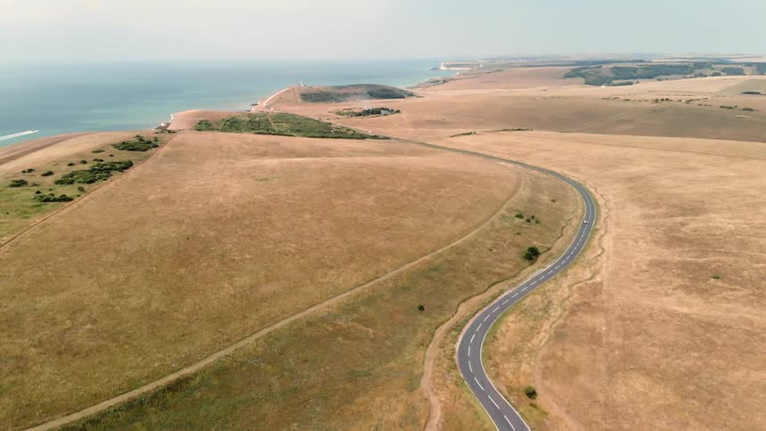 A curvy road next to the ocean is filmed from above