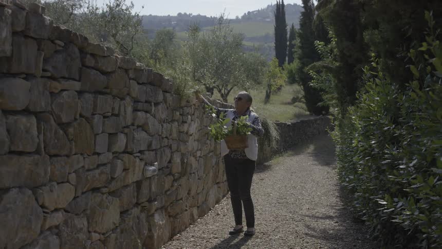 A man walking down a trail picking flowers and collecting them in a basket