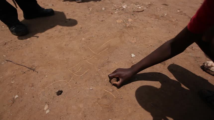 Person carving words into the dirt with a rock