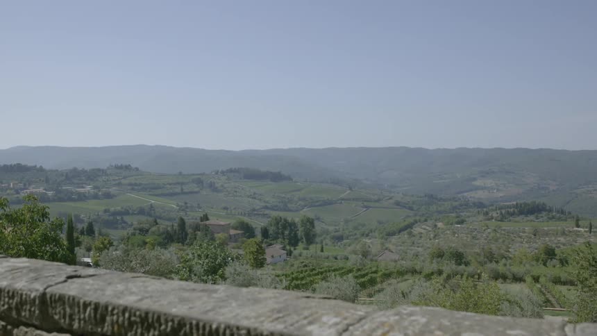 A large wall stands on a hill above a valley full of trees
