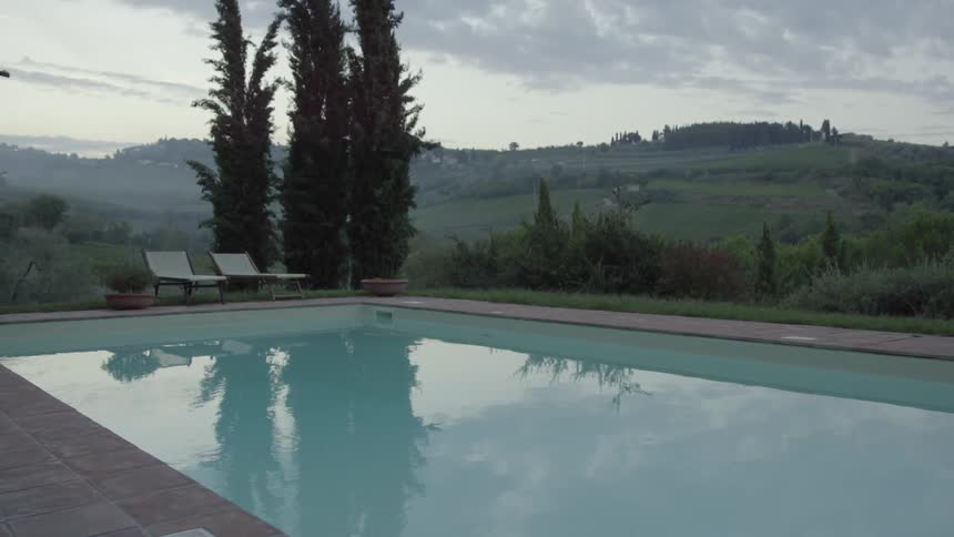 A pool sits empty outside a home in a hilly area on a cloudy day