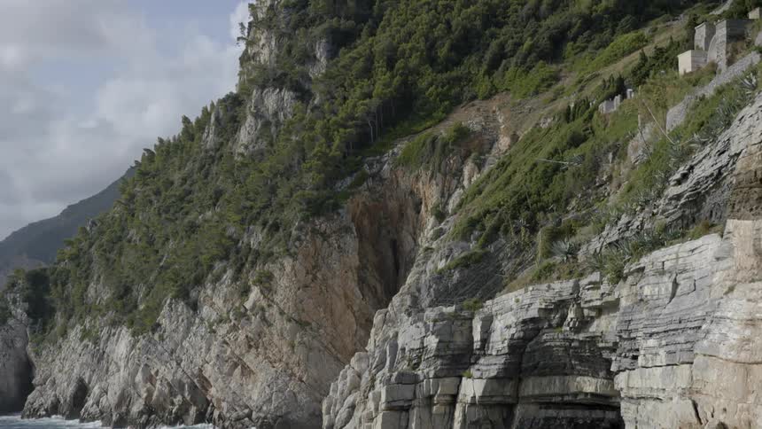 A bird flies out of a cave at the base of the shore of a cliff