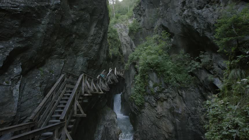 A person leans to peer over a railing on a wooden pathway in a gorge