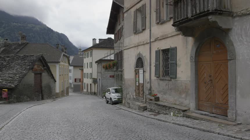 A vehicle sits near buildings in an old european village on a cloudy day