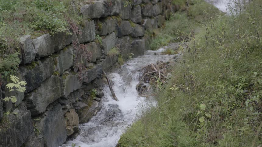 A fast-moving stream flows near a rock wall