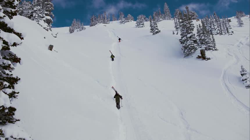 Three people carry their skis as they climb up a mountain slope