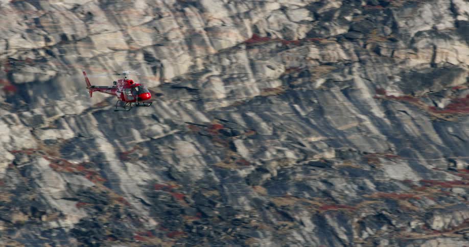 A helicopter is flying above a mountainside during the day