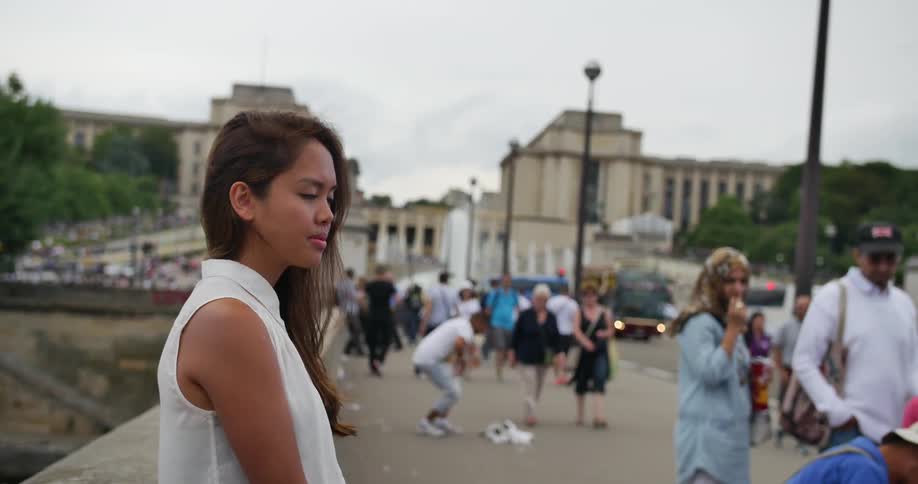 A young asian woman stands against a stone wall on busy city street