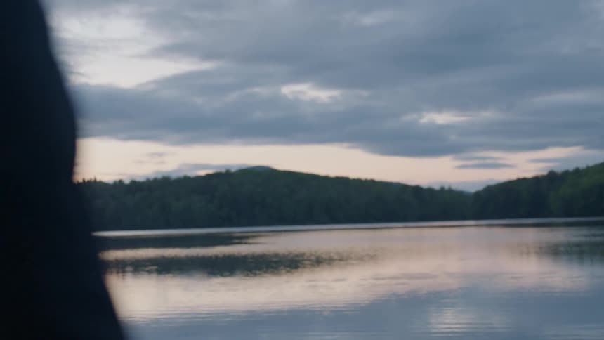 A man watches over the calm lake at sunset