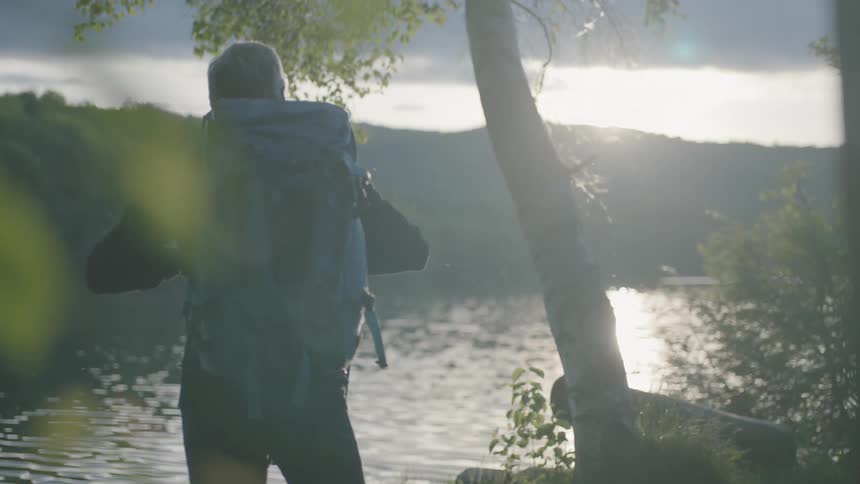 A man wears a backpack near a river