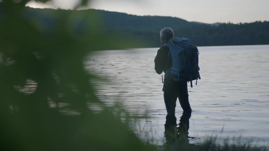 Hiker stands knee deep in a mountain lake