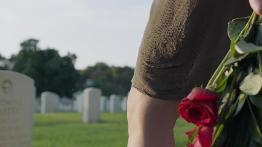 A woman is walking through a graveyard carrying flowers