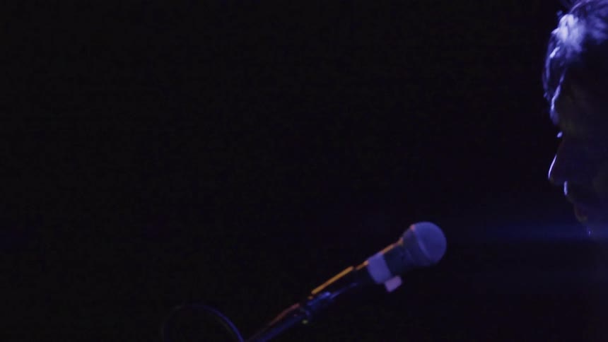 A man leans near the microphone singing on stage