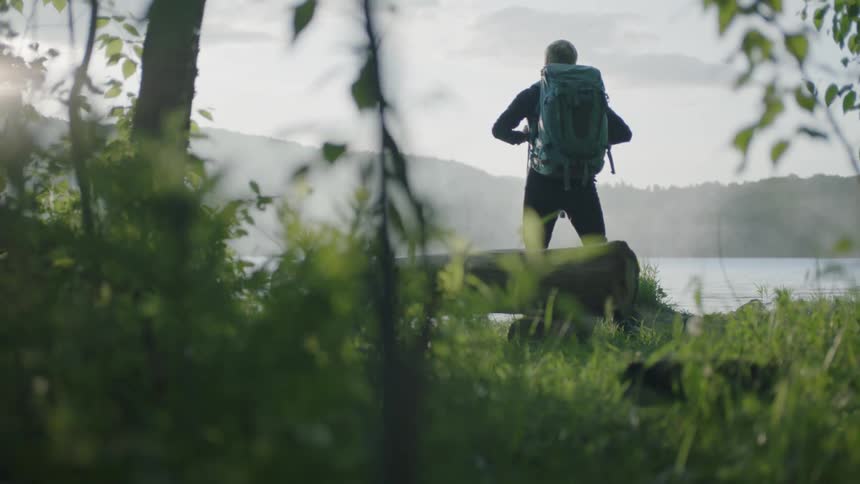 A man wearing a backpack looks out over the lake