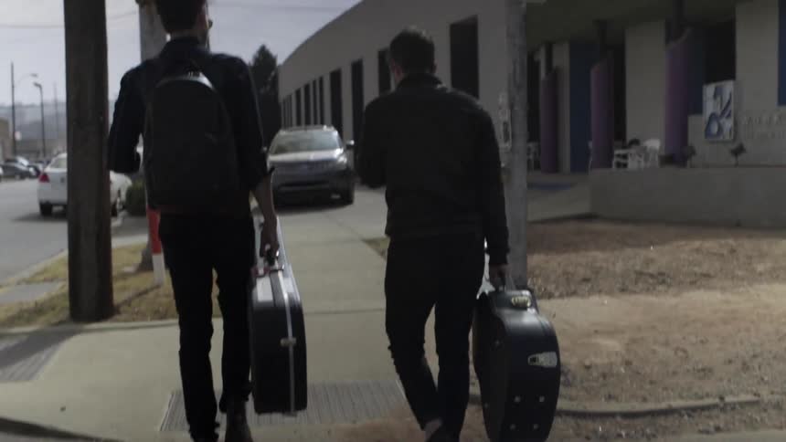 Two guys walking down street sidewalk carrying guitar cases