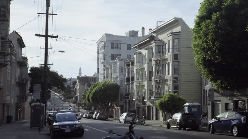 Vehicles parked on a hilly street lined with houses