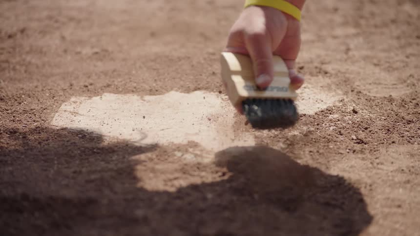 An umpire dusts off home plate on a baseball field