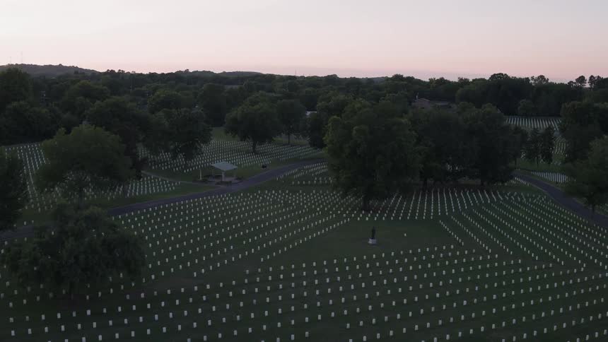 Headstones stand in rows in a cemetery at sunset