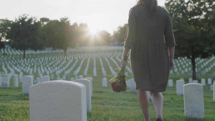 A woman with flowers is walking through a graveyard