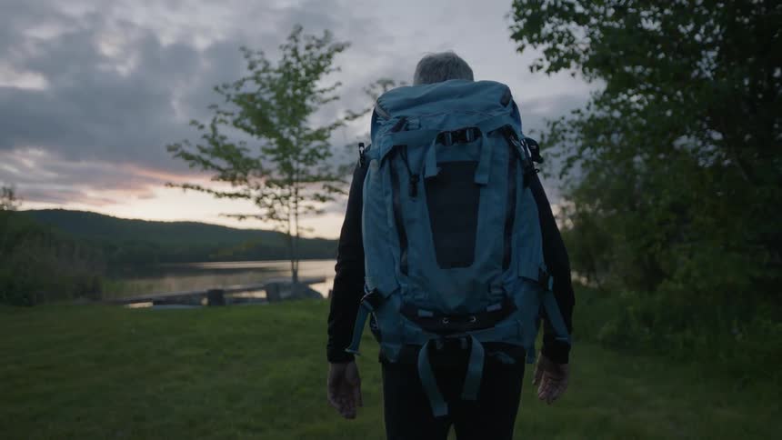A man carries a backpack and walks towards the lake
