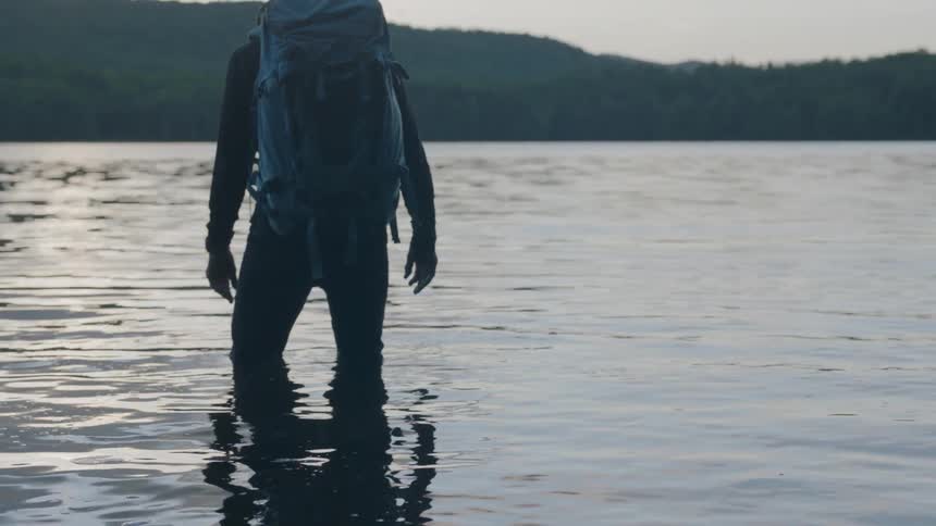 A man with a backpack is standing in knee high water