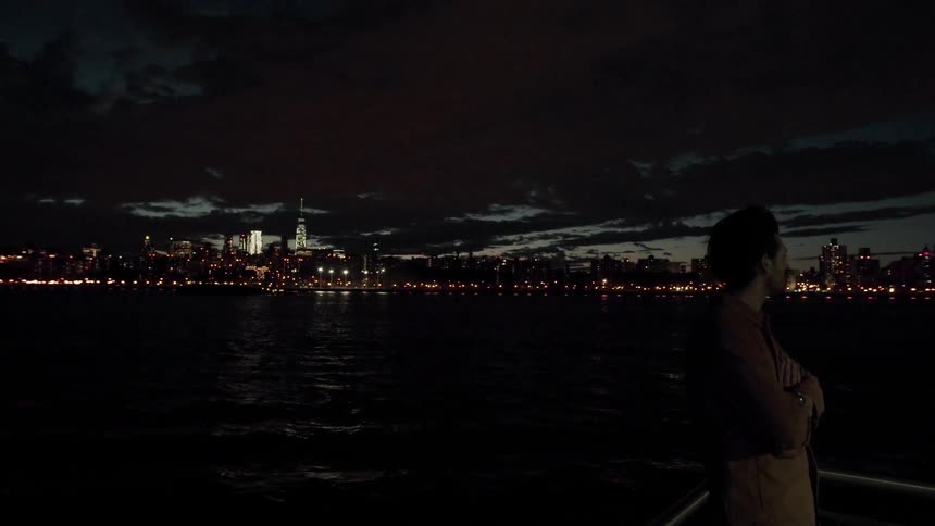 Man looks across river at city night skyline