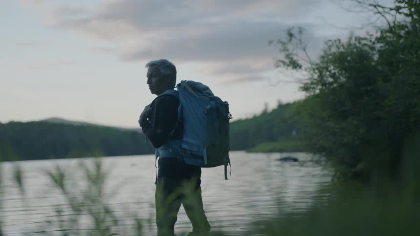 Hiker stands knee deep in a mountain lake at dusk
