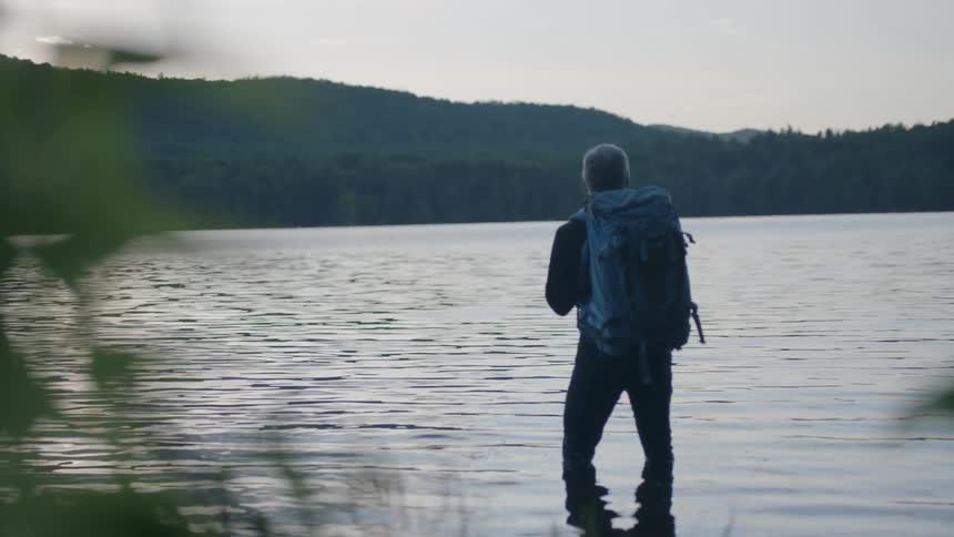 A man with a backpack is knee deep in a lake