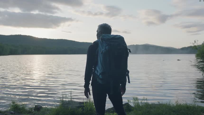 Man wears a backpack as he looks at a lake
