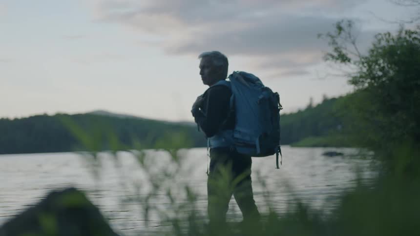A man with a backpack is standing next to a lake