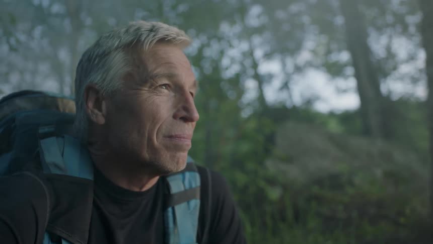 A gray haired man kneeling in a forest