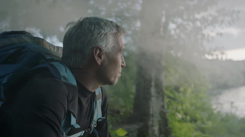 A man with a backpack is kneeling down next to a lake
