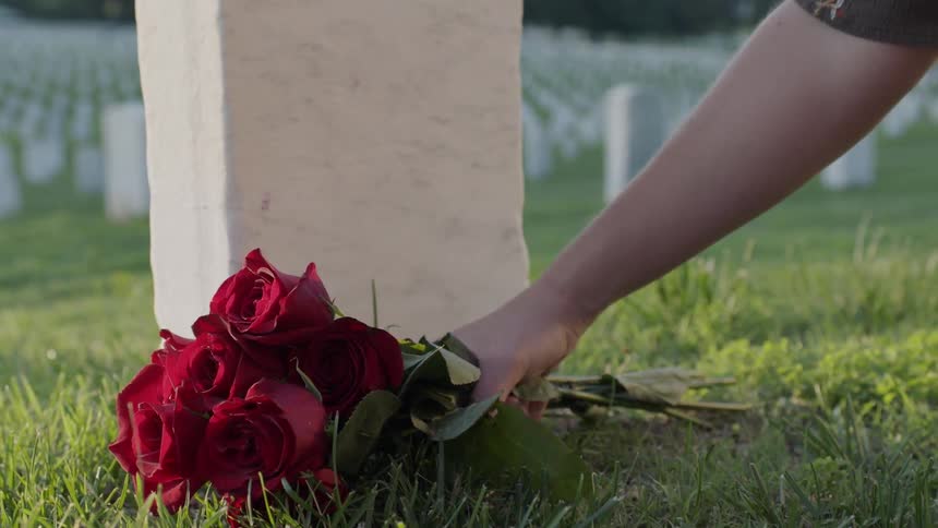 Woman places flowers by a grave