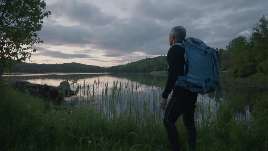 A man walks over to the lake on a cloudy day