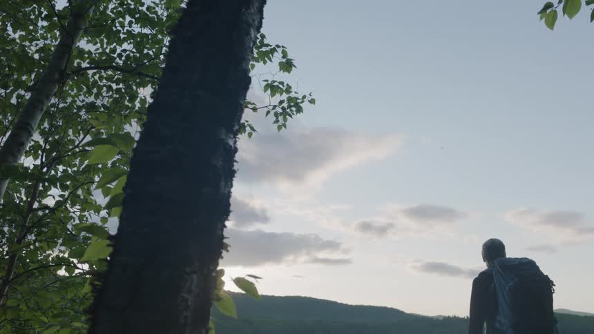 Hiker stands next to a mountain lake at sunset