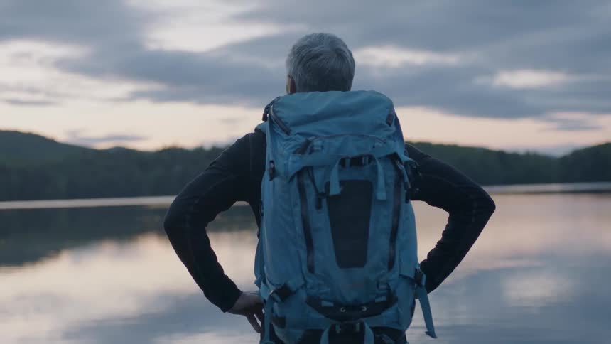 Hiker stands next to a mountain lake at sunset
