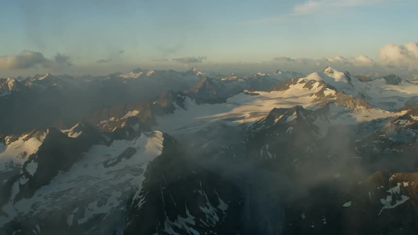 Clouds float over snow covered mountains with glacier