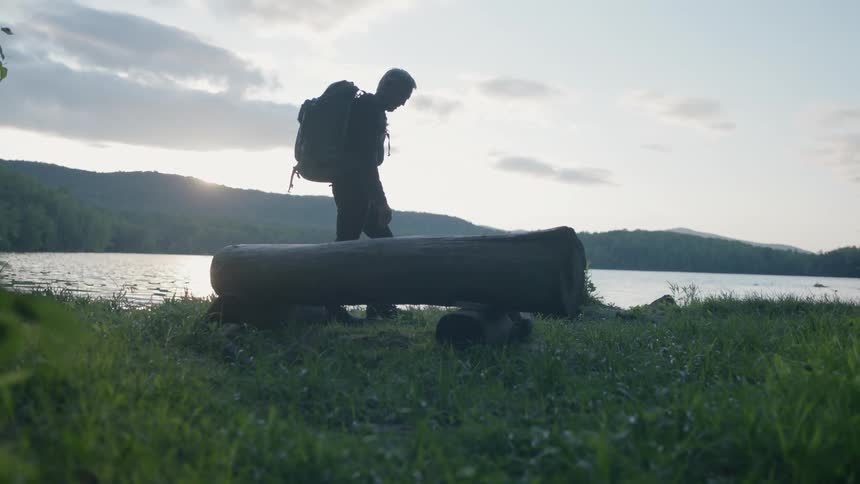 A man walks past the lake with his backpack on before stopping