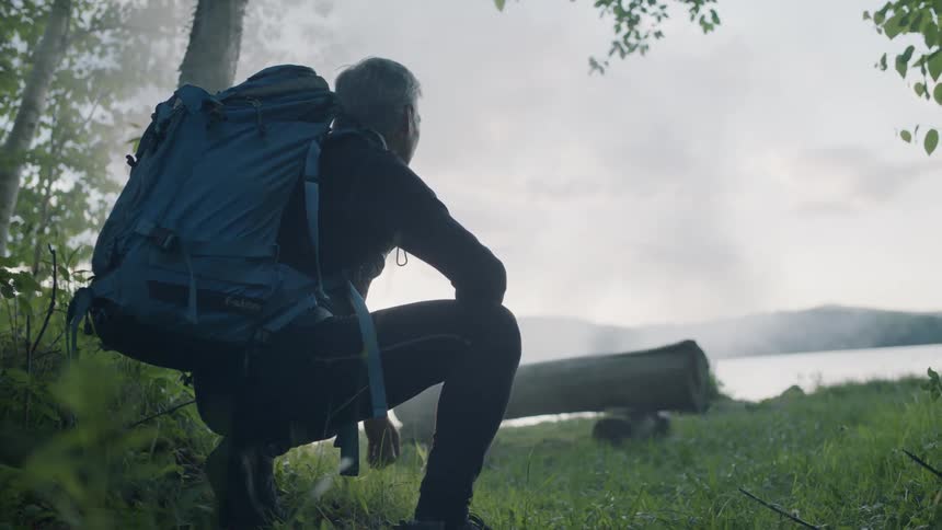A man wearing a backpack and sitting on the rock looking out over the ocean