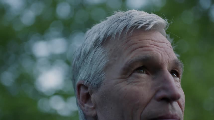 Man with grey hair is outside and staring off