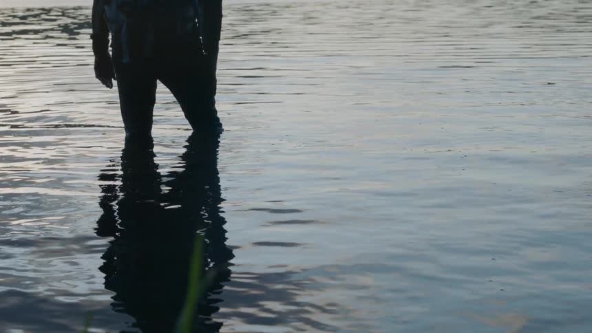 Man stands knee deep in a mountain lake at sunset