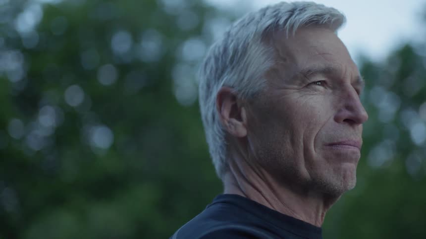 A man is smiling looking forward in front of some trees