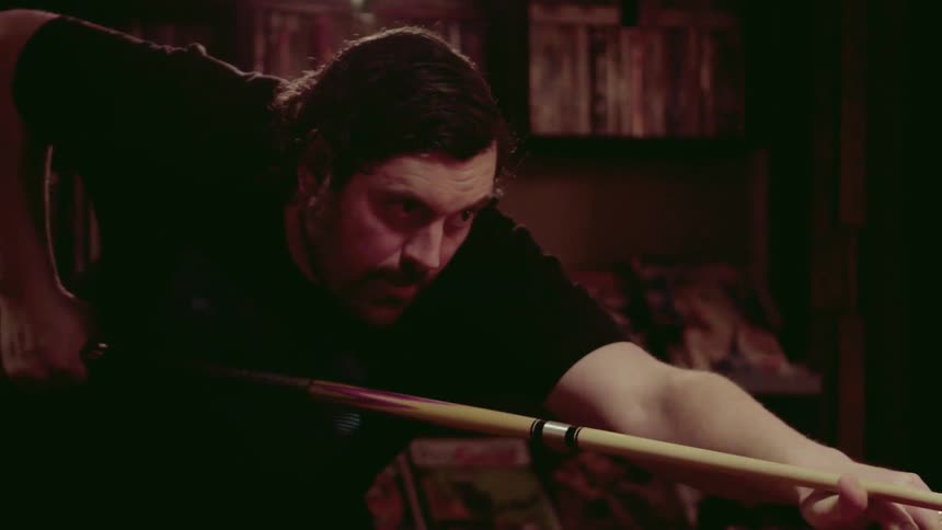 Man aims a pool cue with his thumb
