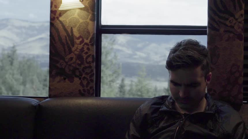 A man is riding in a train going past a mountain