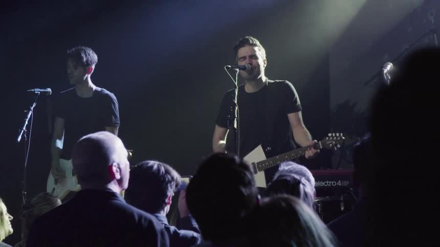 A band is playing on stage to a large crowd that is enjoying it