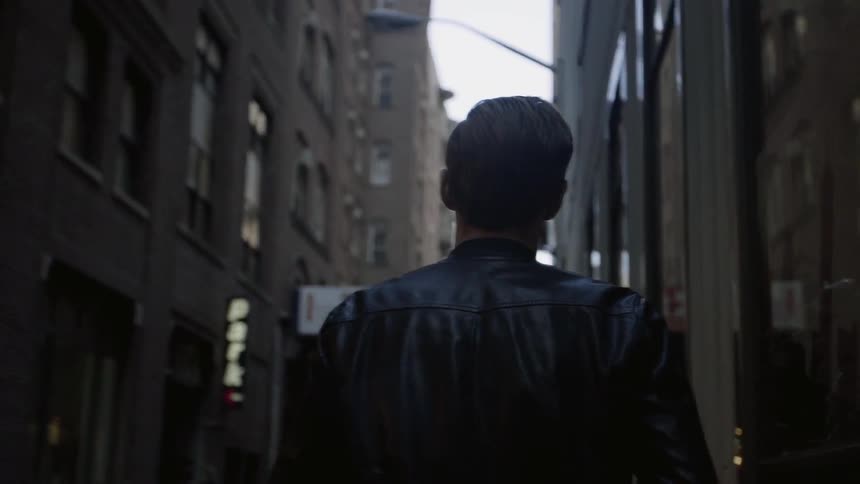 A man in a leather jacket walks between buildings