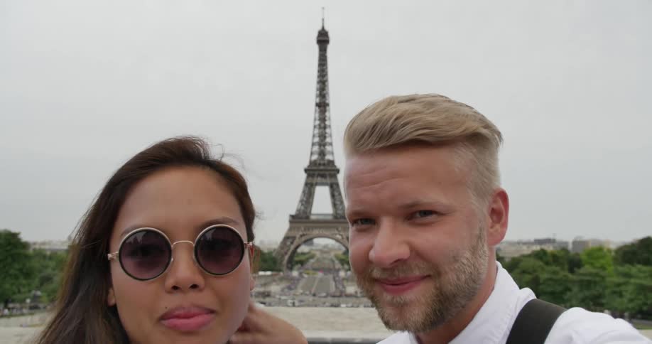A couple pose and kiss in front of the eiffel tower